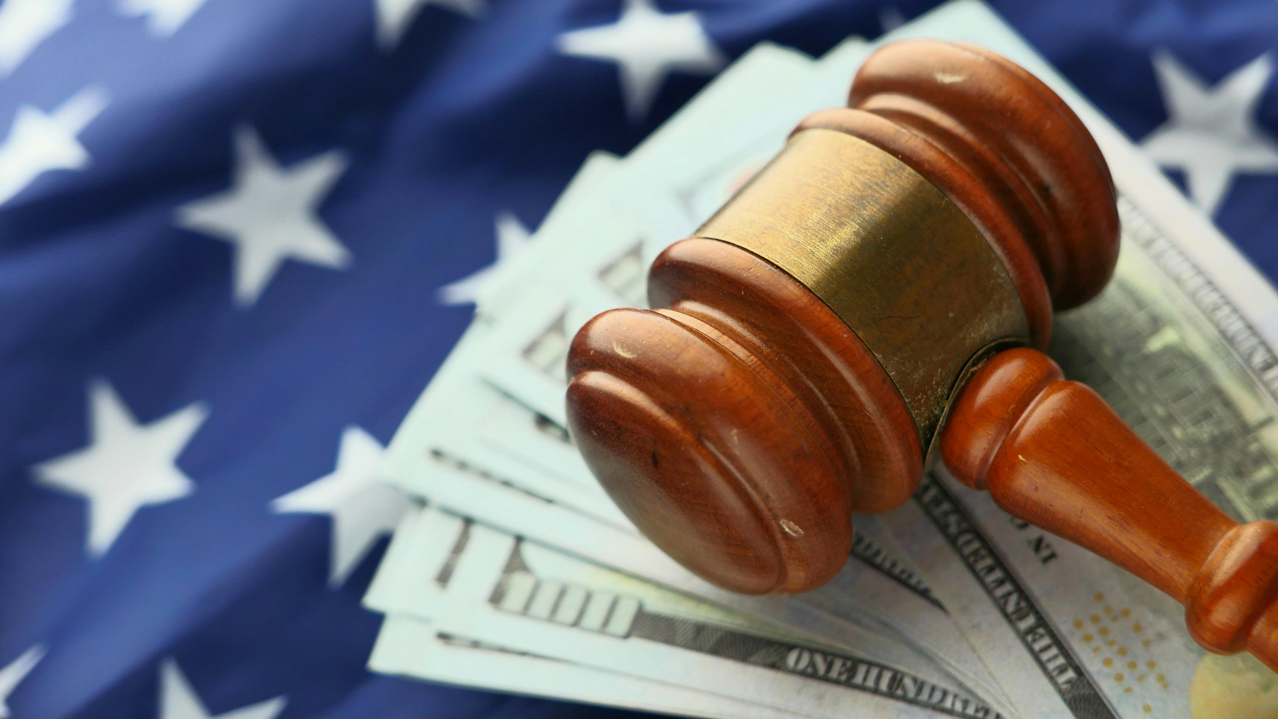 Image principale de l'article : Un marteau de juge en bois posé sur des billets de dollars américains avec un drapeau américain en arrière-plan, symbolisant l'intersection du droit et de la finance dans le système juridique américain.
