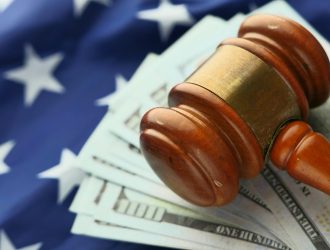 Main article image: A wooden gavel resting on US dollar bills with an American flag in the background, symbolizing the intersection of law and finance in the American legal system.