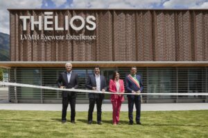 Here are the alt texts for both images in French and English: Image 1: English: "Ribbon-cutting ceremony at the new Thélios metal processing facility in Longarone, with four officials including Regional Councillor Valeria Mantovan in pink suit and local mayor with ceremonial sash standing in front of the modern building with wooden facade and mountain backdrop.