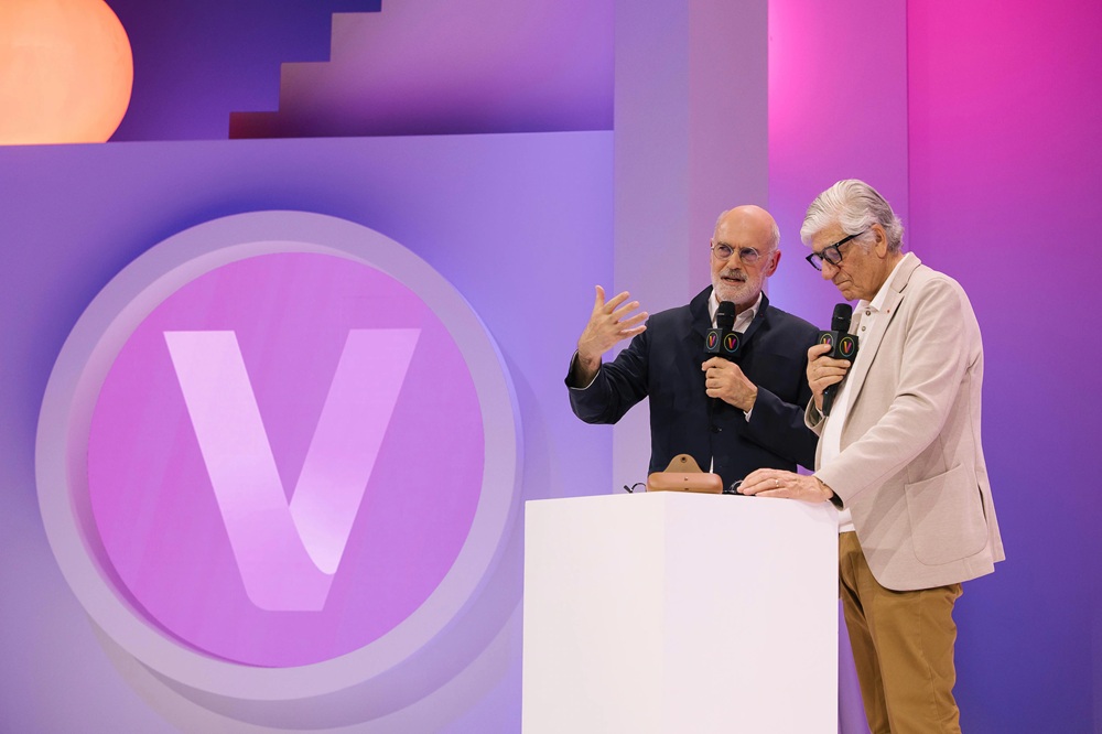 Two speakers presenting at VivaTech 2025 on stage with purple backdrop featuring large "V" logo, both holding microphones during their presentation