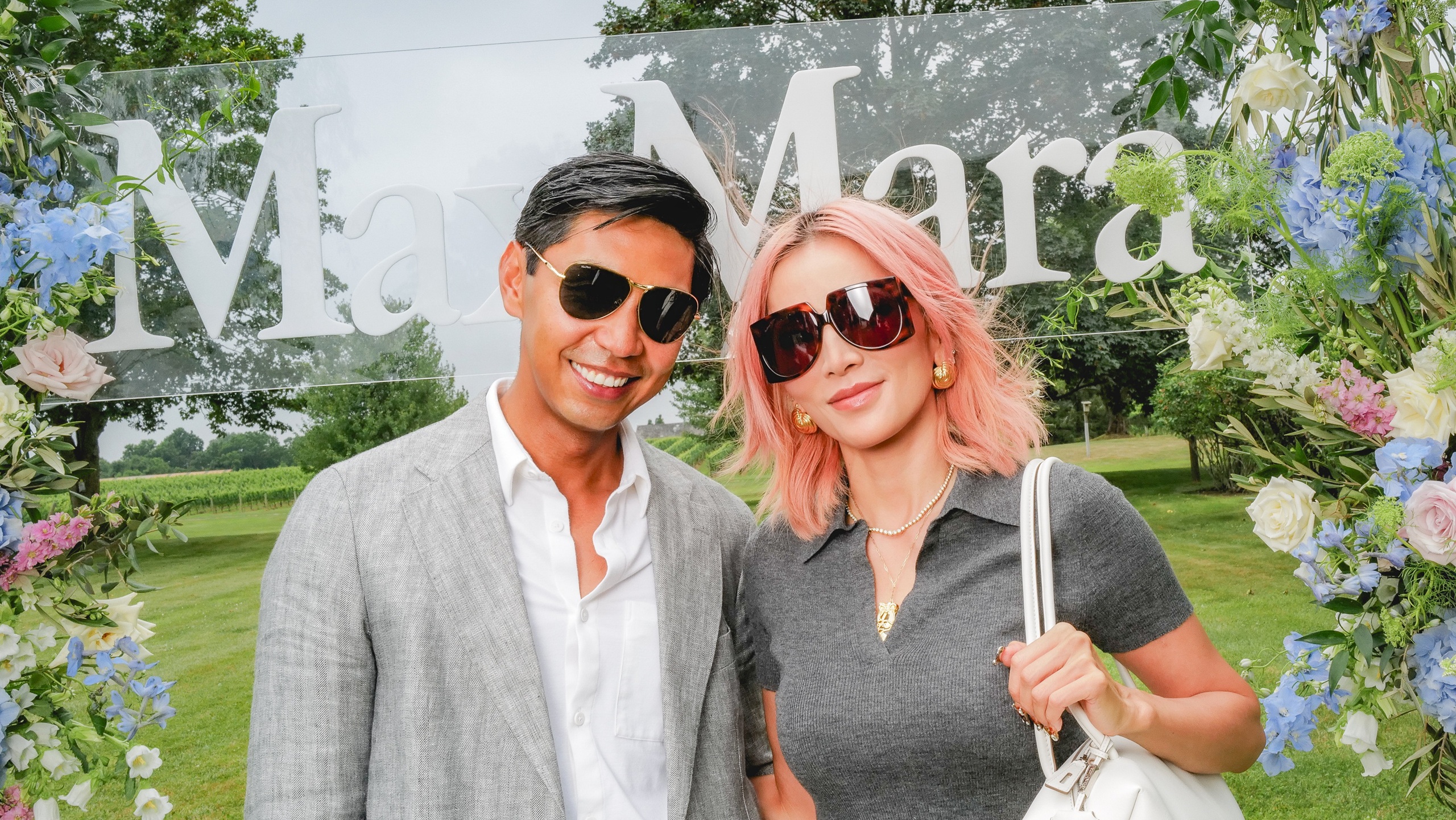Blue Carreon et Tina Leung posent ensemble lors de l'événement lunettes Max Mara, portant toutes deux des lunettes de soleil élégantes de la collection, devant un décor floral avec le logo Max Mara dans un lieu de jardin extérieur.