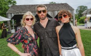 Emily Davis, Maximilian Eicke et Irina Kro Eicke (de gauche à droite) assistent au déjeuner lunettes Max Mara, portant tous des lunettes de soleil de la collection, photographiés en extérieur au lieu des Hamptons avec des bâtiments rustiques en arrière-plan.
