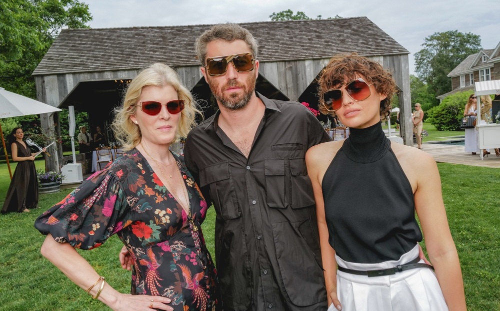 Emily Davis, Maximilian Eicke et Irina Kro Eicke (de gauche à droite) assistent au déjeuner lunettes Max Mara, portant tous des lunettes de soleil de la collection, photographiés en extérieur au lieu des Hamptons avec des bâtiments rustiques en arrière-plan.