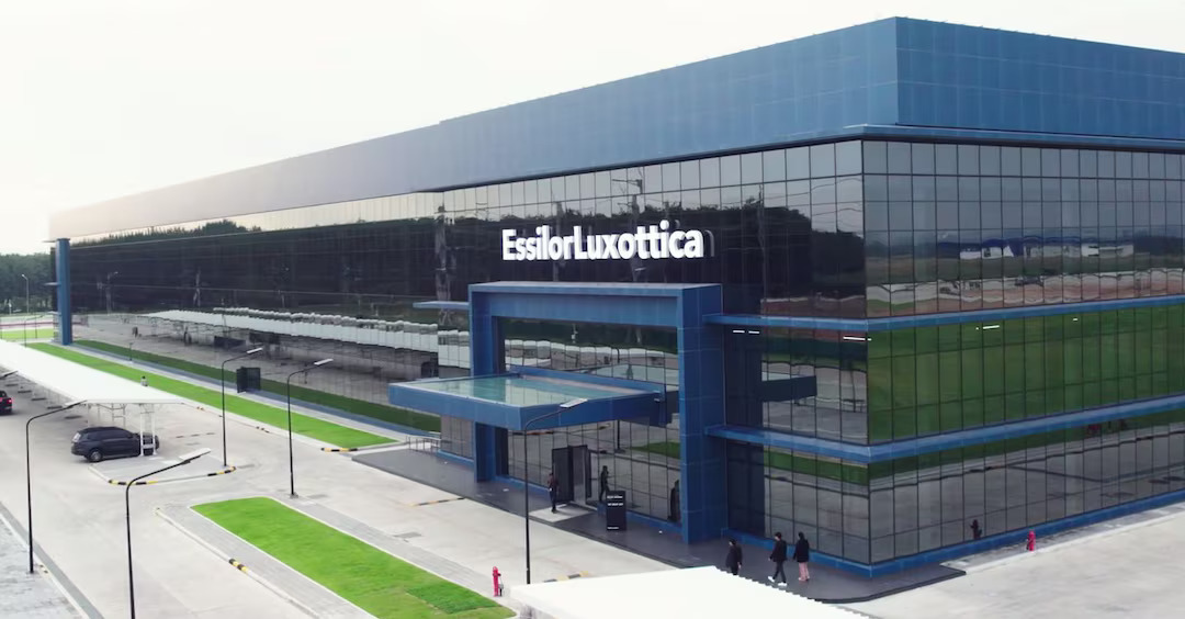 Installations corporatives modernes d'EssilorLuxottica avec une architecture contemporaine en verre et acier présentant des accents bleus et verts, de grandes fenêtres, et le nom de l'entreprise affiché de manière proéminente sur l'extérieur du bâtiment.