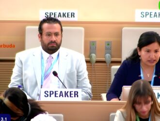L'image montre une salle de réunion de l'Assemblée mondiale de la santé avec deux orateurs aux podiums - un homme en costume blanc et lunettes à gauche, et une femme en blazer bleu marine à droite. Le cadre est celui de la 78e Assemblée mondiale de la santé où la résolution sur les déficiences sensorielles était en discussion.