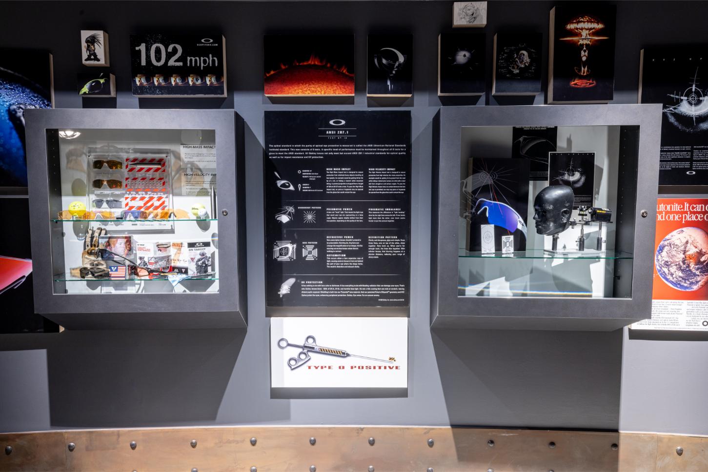Vitrines d'exposition dans les archives MUZM 2.0 d'Oakley présentant des lunettes historiques, accessoires et objets de collection avec des panneaux informatifs sur l'héritage de la marque et un affichage de vitesse '102 mph'.