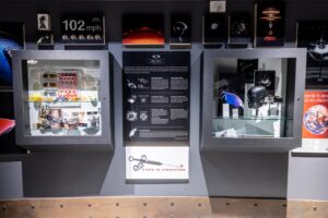 Display cases in Oakley's MUZM 2.0 archive featuring historical eyewear, accessories, and memorabilia with informational panels about the brand's legacy and a '102 mph' speed measurement display.