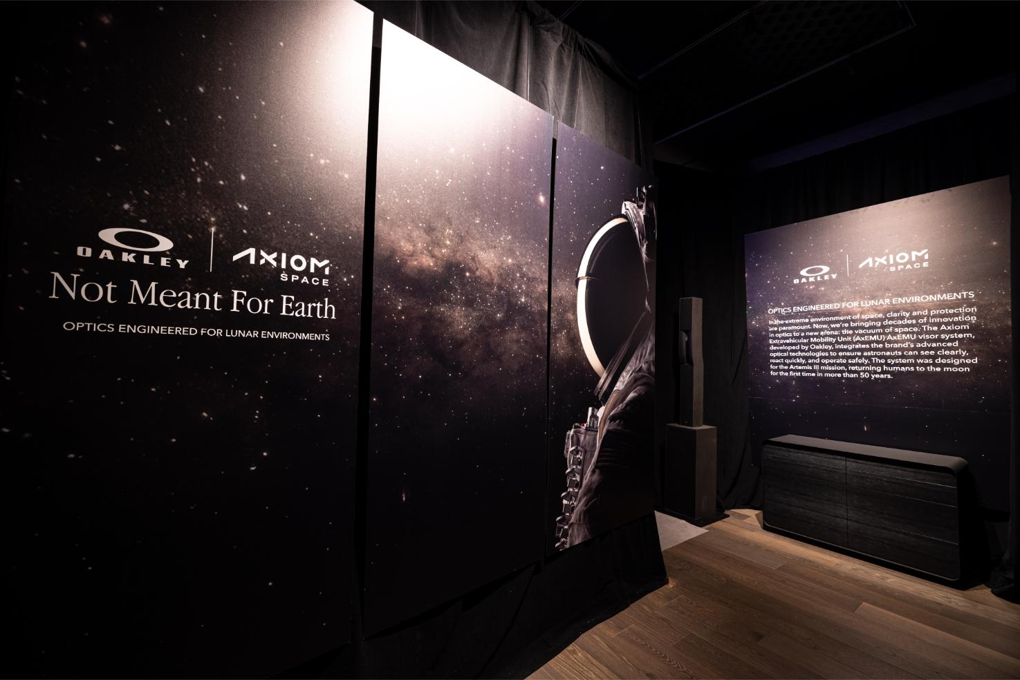 Exposition de l'expérience Oakley Axiom Space avec un arrière-plan de champ d'étoiles cosmiques, le branding 'Not Meant For Earth' et un casque de combinaison spatiale présentant l'optique conçue pour les environnements lunaires.