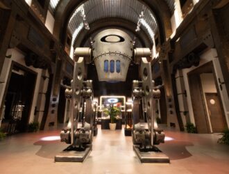 Futuristic Oakley headquarters entrance featuring a large metallic robot-like sculpture with the Oakley logo, industrial design elements, and dramatic lighting in an atrium setting.