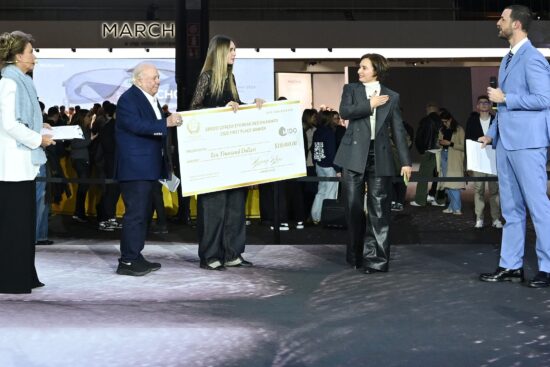 Cérémonie de remise de prix au MIDO 2025 montrant la présentation du Prix de Design Lunetterie Sergio Cereda. Un grand chèque cérémonial de 10 000 $ est remis au gagnant de la première place, avec plusieurs officiels en tenue formelle participant à la présentation sur scène.