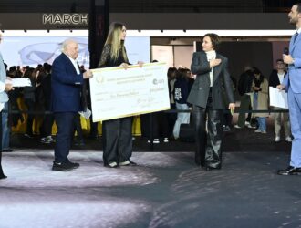 Award ceremony at MIDO 2025 showing the presentation of the Sergio Cereda Eyewear Design Award. A large ceremonial check for $10,000 is being presented to the first place winner, with several officials in formal attire participating in the presentation on stage.