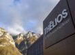 Vue extérieure de l'installation Thélios LVMH Eyewear Excellence à Longarone, montrant le bâtiment moderne sombre avec la signalétique de l'entreprise sur le fond dramatique des montagnes des Dolomites italiennes.