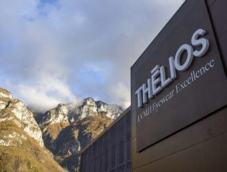 Vue extérieure de l'installation Thélios LVMH Eyewear Excellence à Longarone, montrant le bâtiment moderne sombre avec la signalétique de l'entreprise sur le fond dramatique des montagnes des Dolomites italiennes.