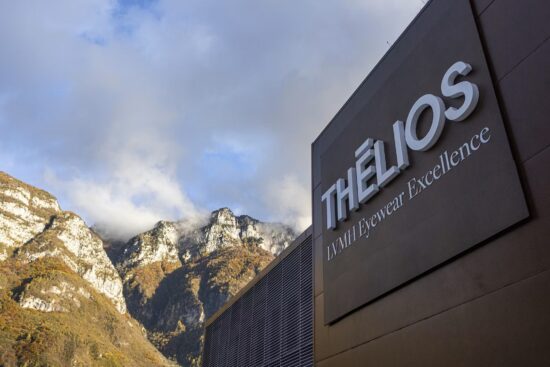 Vue extérieure de l'installation Thélios LVMH Eyewear Excellence à Longarone, montrant le bâtiment moderne sombre avec la signalétique de l'entreprise sur le fond dramatique des montagnes des Dolomites italiennes.
