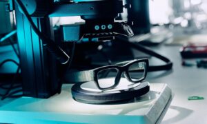 Smart glasses positioned on a circular testing platform under precision laboratory equipment, demonstrating the advanced testing and quality control processes in EssilorLuxottica's smart eyewear development laboratory.