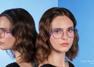 Campaign image for Face à Face, showing a woman wearing colorful geometric eyeglasses in blue and orange, standing beside a mirror that reflects her profile against a gradient blue background.