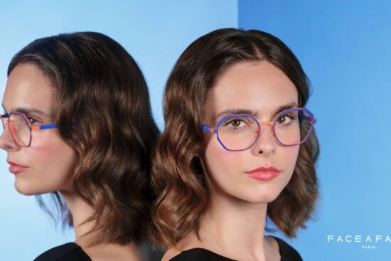 Campaign image for Face à Face, showing a woman wearing colorful geometric eyeglasses in blue and orange, standing beside a mirror that reflects her profile against a gradient blue background.
