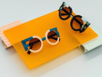 Présentation artistique de lunettes de soleil FACE A FACE sur des plateformes acryliques colorées - deux paires de lunettes avant-gardistes aux montures géométriques en rose, bleu et noir disposées sur des surfaces translucides orange vif, pêche et vert menthe.
