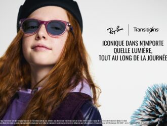 Une jeune fille aux longs cheveux roux-brun portant un béret noir et des lunettes de soleil Ray-Ban à monture violette avec des verres Transitions teintés. Elle regarde directement vers l'appareil photo avec une légère expression neutre. L'image inclut les logos Ray-Ban et Transitions avec le texte 'ICONIQUE DANS N'IMPORTE QUELLE LUMIÈRE, TOUT AU LONG DE LA JOURNÉE' et un objet décoratif épineux bleu et noir visible dans le coin inférieur droit. Du texte légal en français apparaît en bas de l'image.