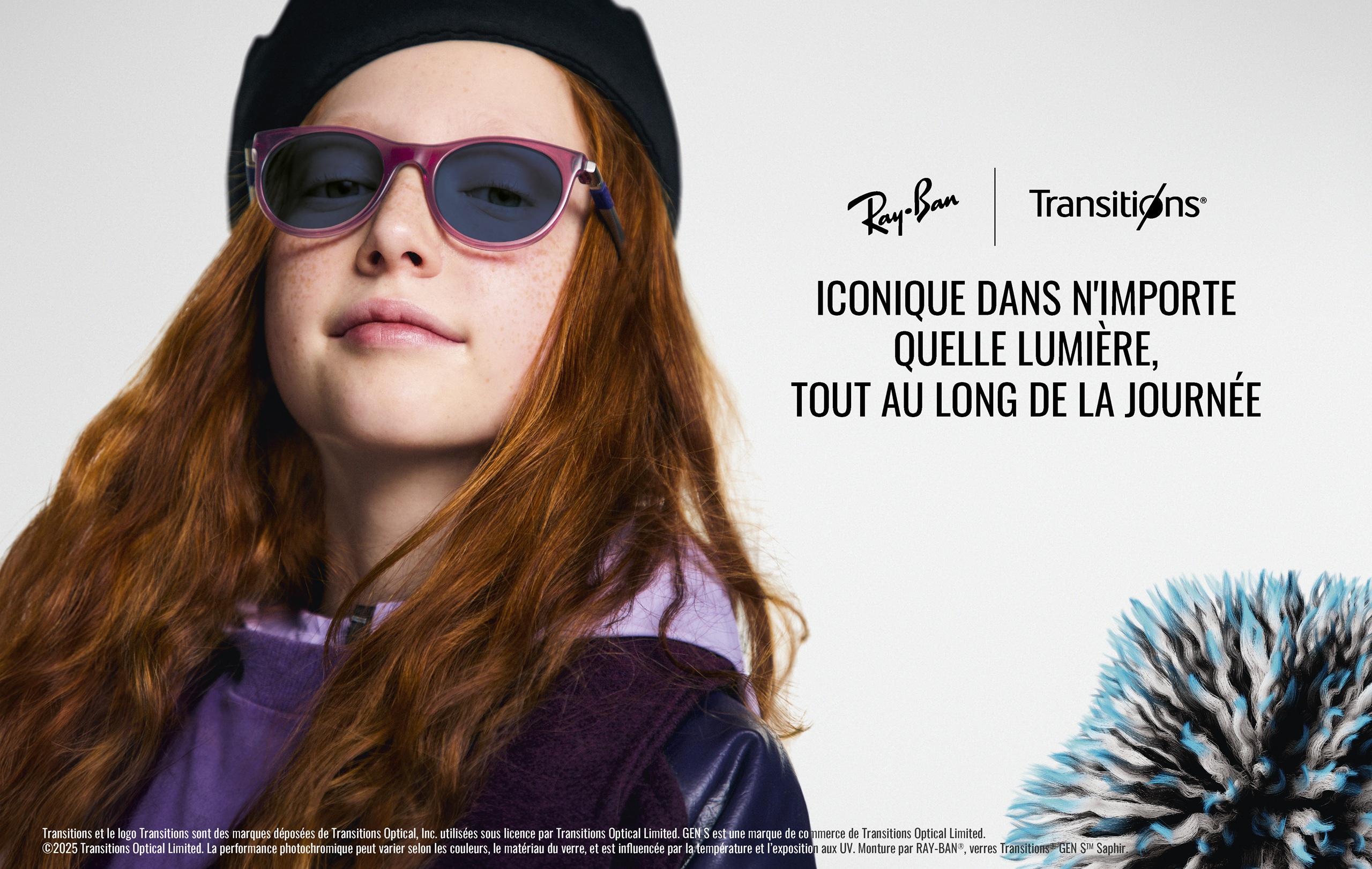Une jeune fille aux longs cheveux roux-brun portant un béret noir et des lunettes de soleil Ray-Ban à monture violette avec des verres Transitions teintés. Elle regarde directement vers l'appareil photo avec une légère expression neutre. L'image inclut les logos Ray-Ban et Transitions avec le texte 'ICONIQUE DANS N'IMPORTE QUELLE LUMIÈRE, TOUT AU LONG DE LA JOURNÉE' et un objet décoratif épineux bleu et noir visible dans le coin inférieur droit. Du texte légal en français apparaît en bas de l'image.