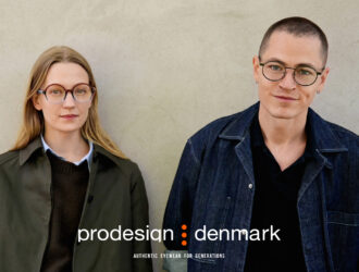Deux personnes portant des lunettes Prodesign Denmark debout contre un mur de béton. À gauche, une femme aux cheveux blonds portant des lunettes rondes écaille de tortue et une veste vert olive. À droite, une personne aux cheveux courts portant des lunettes rondes à monture noire et une veste en denim foncé. Le logo Prodesign Denmark et le slogan 'Authentic Eyewear for Generations' apparaissent en bas.