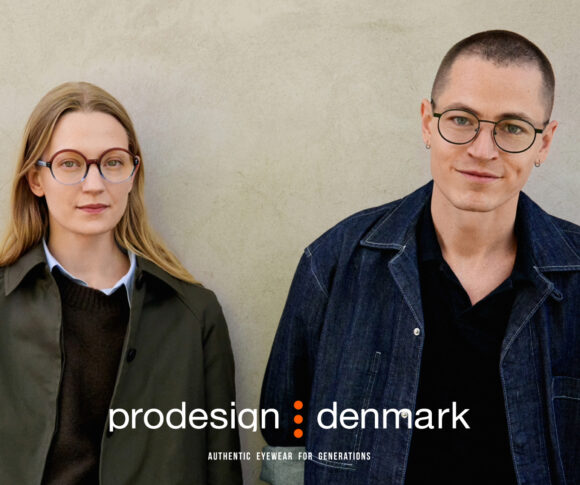 Deux personnes portant des lunettes Prodesign Denmark debout contre un mur de béton. À gauche, une femme aux cheveux blonds portant des lunettes rondes écaille de tortue et une veste vert olive. À droite, une personne aux cheveux courts portant des lunettes rondes à monture noire et une veste en denim foncé. Le logo Prodesign Denmark et le slogan 'Authentic Eyewear for Generations' apparaissent en bas.