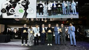 MIDO awards ceremony showing a group of award winners standing on stage holding golden trophy awards, with a large screen behind them displaying the event branding including Best Store Award, Stand Up For Green 2025, CSE Award 2025, and MIDO logos alongside images of eyewear models.