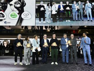 MIDO awards ceremony showing a group of award winners standing on stage holding golden trophy awards, with a large screen behind them displaying the event branding including Best Store Award, Stand Up For Green 2025, CSE Award 2025, and MIDO logos alongside images of eyewear models.