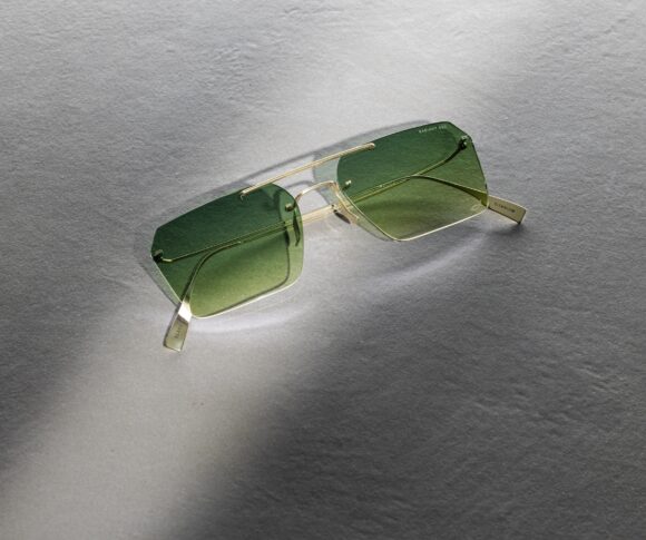 Lunettes de soleil Blackfin Aero Loop Infinity avec verres carrés géométriques et dégradé vert, présentant une construction en titane ultra-minimaliste avec design de pont géométrique, photographiées sur une surface grise texturée