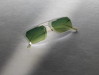 Blackfin Aero Loop Infinity sunglasses with geometric squared lenses and green gradient tinting, featuring ultra-minimalist titanium construction with geometric bridge design, photographed on a textured grey surface