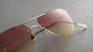 Close-up detail of Blackfin Aero Loop Infinity aviator sunglasses showcasing the patented rimless design with fluid titanium bridge, pink-to-amber gradient lenses, and precision-sculpted titanium components with polished finish
