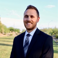 Professional headshot of Michael Gatti with dark hair and beard in navy suit and tie, smiling outdoors with golf course in background