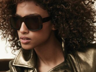 Mannequin aux cheveux bouclés volumineux portant des lunettes de soleil Donna Karan et une veste en cuir doré métallisé, photographiée en éclairage naturel pour la campagne Automne 2025