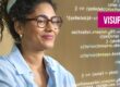Une jeune femme noire aux cheveux bouclés sourit en regardant l'écran d'un ordinateur. Elle porte une chemise bleu clair à col et des lunettes. L'écran affiche des lignes de code et le logo stylisé de « VISUPRO » apparaît dans le coin supérieur droit.