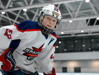 Hockey player wearing white, blue and red uniform with protective helmet and face cage on an indoor ice rink