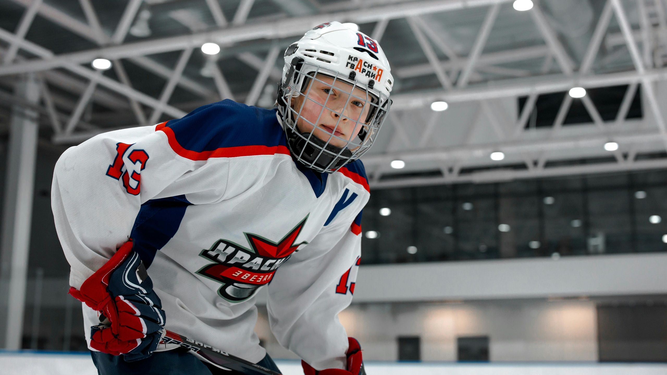 Hockey player wearing white, blue and red uniform with protective helmet and face cage on an indoor ice rink