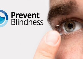 Close-up of a person's eye and finger as they insert or remove a contact lens, with the Prevent Blindness logo (featuring a circular design in blue, green, and yellow tones) displayed prominently in the upper left corner of the image.