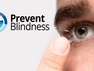 Close-up of a person's eye and finger as they insert or remove a contact lens, with the Prevent Blindness logo (featuring a circular design in blue, green, and yellow tones) displayed prominently in the upper left corner of the image.