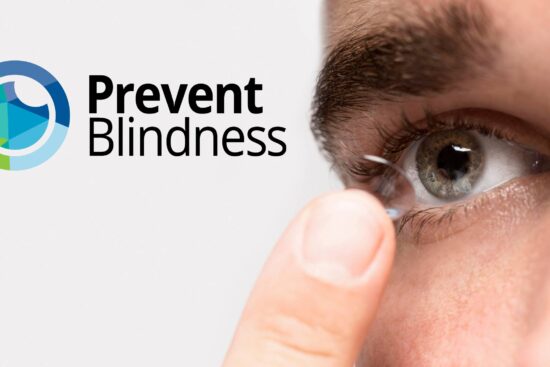 Close-up of a person's eye and finger as they insert or remove a contact lens, with the Prevent Blindness logo (featuring a circular design in blue, green, and yellow tones) displayed prominently in the upper left corner of the image.
