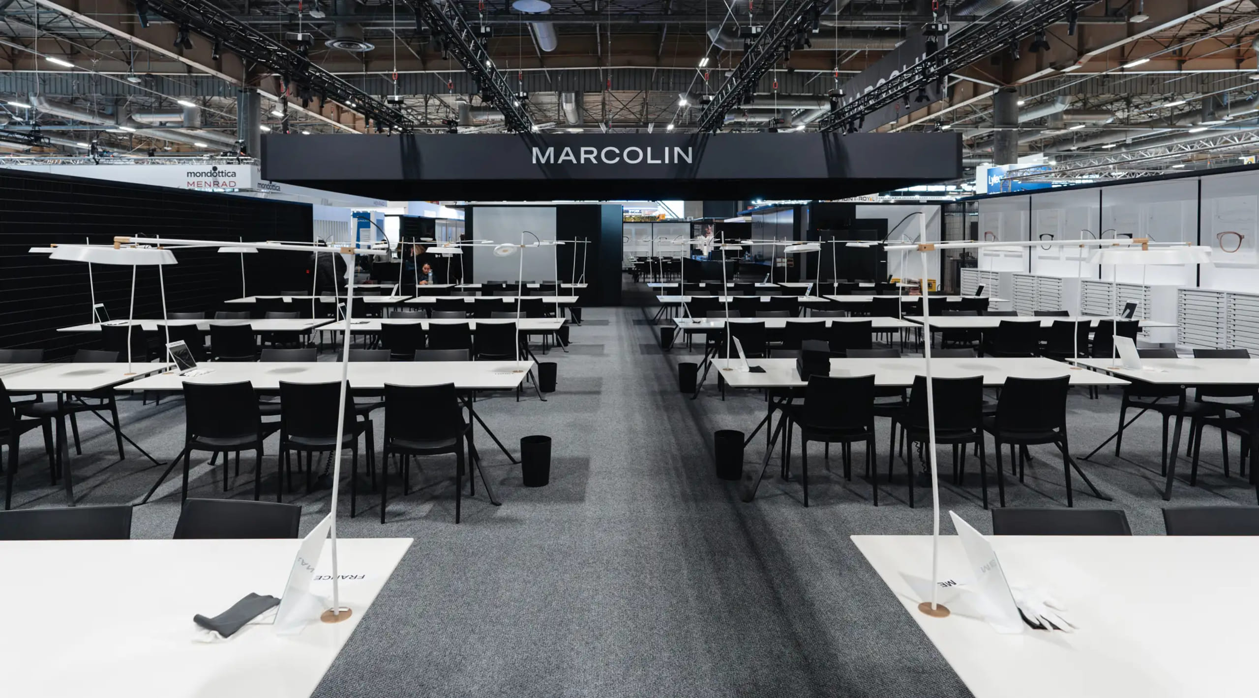 Stand d'exposition Marcolin au SILMO 2025 Paris avec design minimaliste moderne, tables d'exposition blanches et chaises noires dans le Hall 6