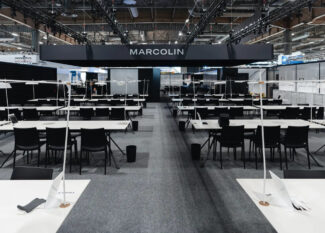 Marcolin exhibition booth at SILMO 2025 Paris featuring modern minimalist design with white display tables and black chairs in Hall 6