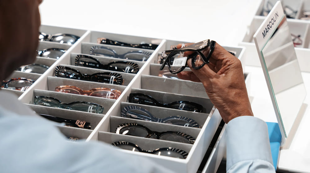 Main examinant des montures de lunettes dans des présentoirs organisés au stand Marcolin lors du salon SILMO Paris 2025