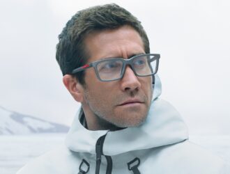 Jake Gyllenhaal portant des lunettes Prada Linea Rossa en équipement d'hiver blanc sur fond de montagne brumeuse
