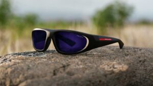 Lunettes de soleil enveloppantes Prada Linea Rossa avec verres teintés bleus et détails argentés sur surface de pierre