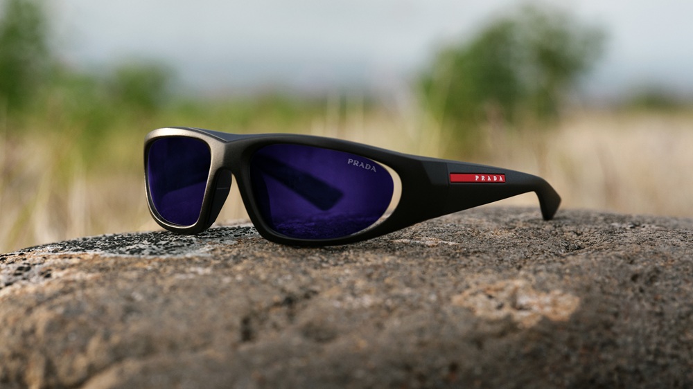 Lunettes de soleil enveloppantes Prada Linea Rossa avec verres teintés bleus et détails argentés sur surface de pierre