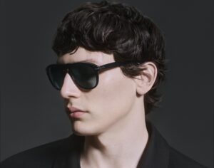 Male model Filipe Nieves in profile wearing Persol Total Black Arrow sunglasses with black clothing, highlighting the frame's sculptural design and cinematic aesthetic
