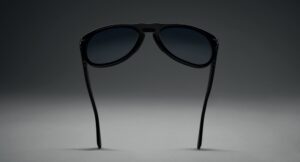 Lunettes de soleil Persol Total Black Arrow vues de dos, présentant la monture entièrement noire et les branches sur un fond dégradé gris