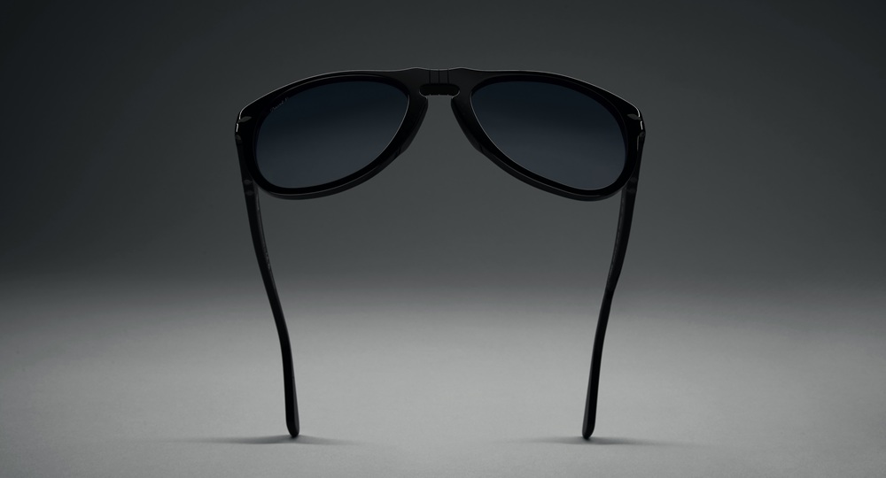 Lunettes de soleil Persol Total Black Arrow vues de dos, présentant la monture entièrement noire et les branches sur un fond dégradé gris
