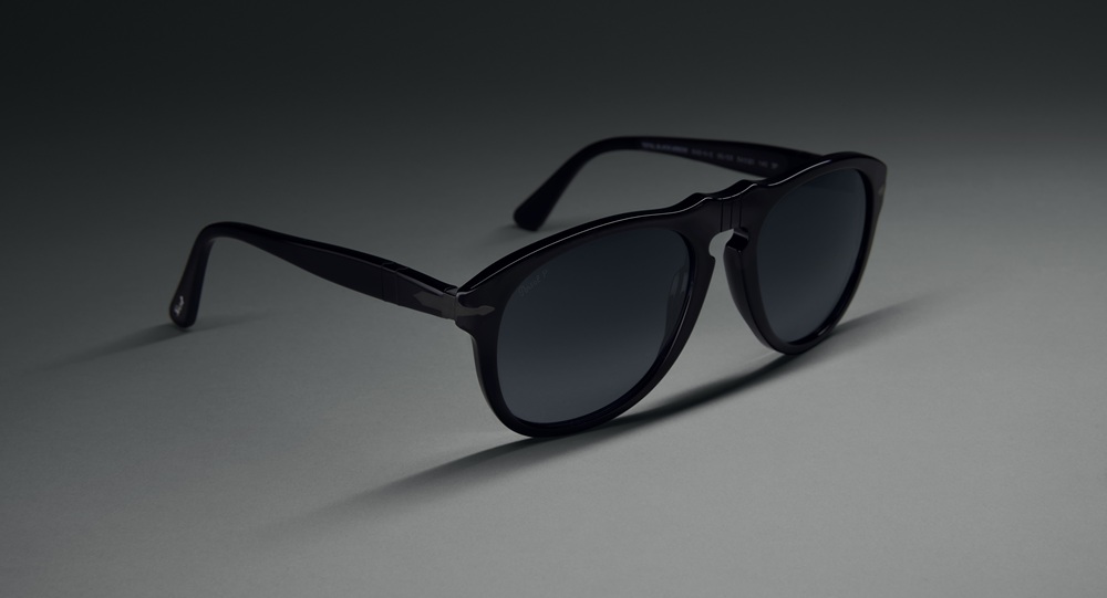 Lunettes de soleil Persol 0PO0649NE Total Black Arrow en silhouette pilote classique avec la charnière fléchée distinctive, photographiées en angle sur fond gris