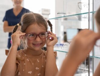 Young girl with braids trying on red eyeglasses at optometrist office